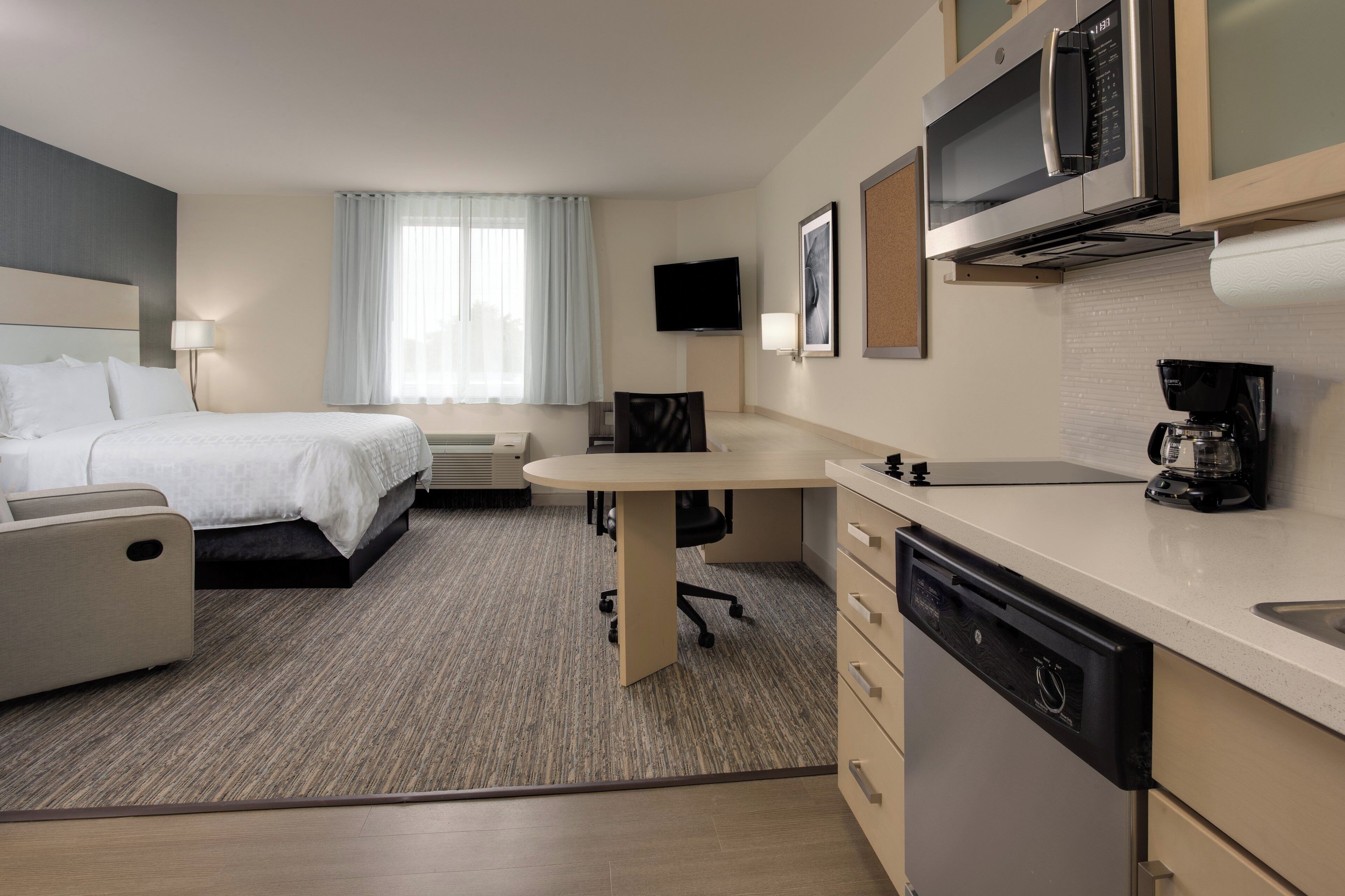 A hotel room with a bed, a desk, a chair, a television, a coffee maker, and a microwave.