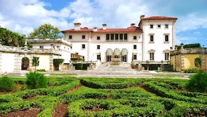 A large, historic building with a symmetrical facade, a central entrance with a staircase, and a formal garden with neatly trimmed hedges in front. - Candlewood Suites Miami Intl Airport - 36th St by IHG (Miami)