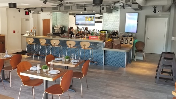 A modern restaurant with a bar area, wooden tables, and bar stools. - Candlewood Suites Miami Intl Airport - 36th St by IHG (Miami)