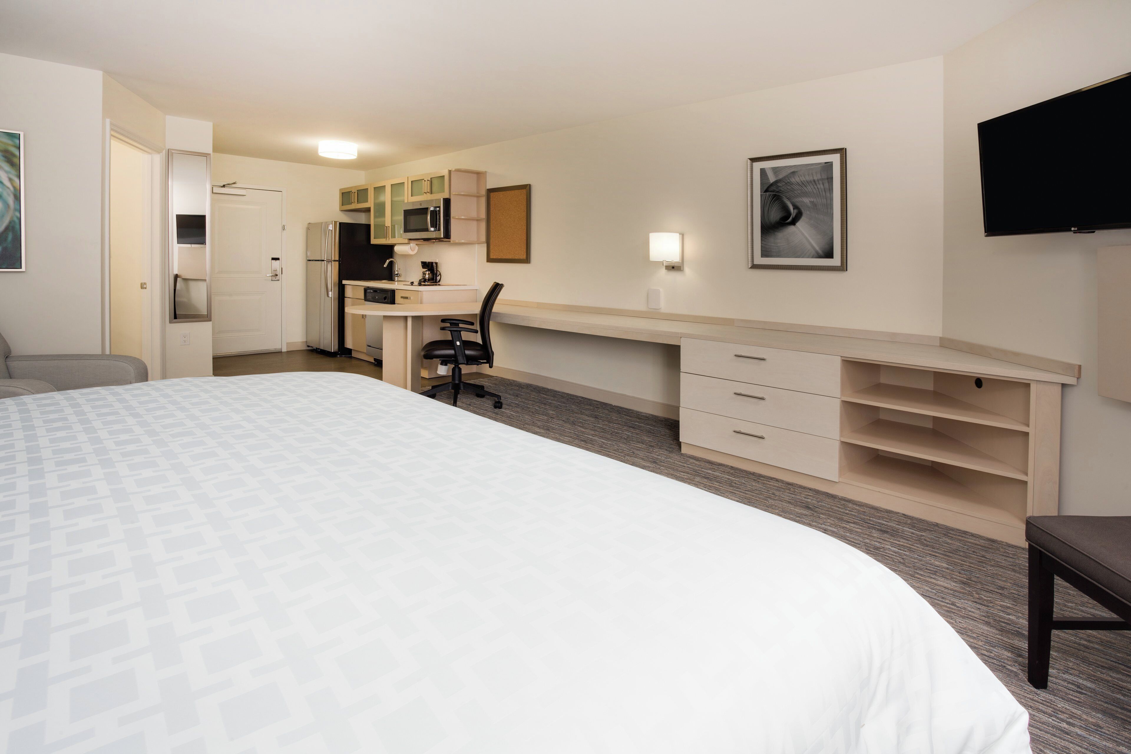 Habitación de hotel con cama, escritorio, silla, televisión y kitchenette.