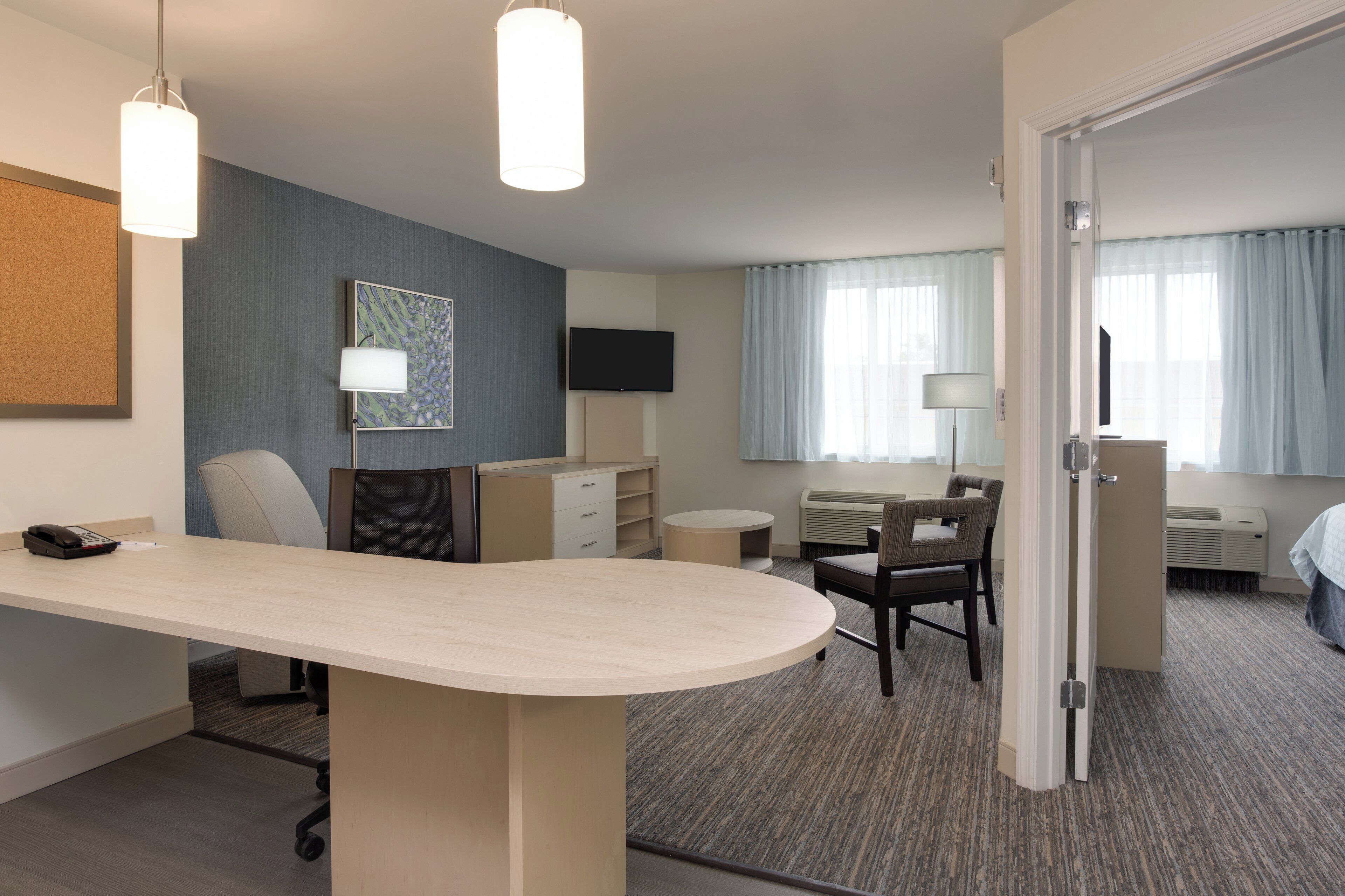 Habitación de hotel con escritorio, sillas, televisor de pantalla plana, cama y puerta que conduce a otra habitación.