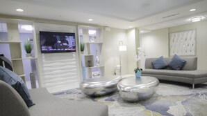 A modern living room with a sofa, two round coffee tables, a flat-screen TV, and decorative plants. - Candlewood Suites Miami Intl Airport - 36th St by IHG (Miami)