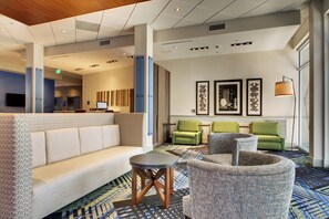 A hotel lobby with a sofa, armchairs, a small table, and artwork on the walls.