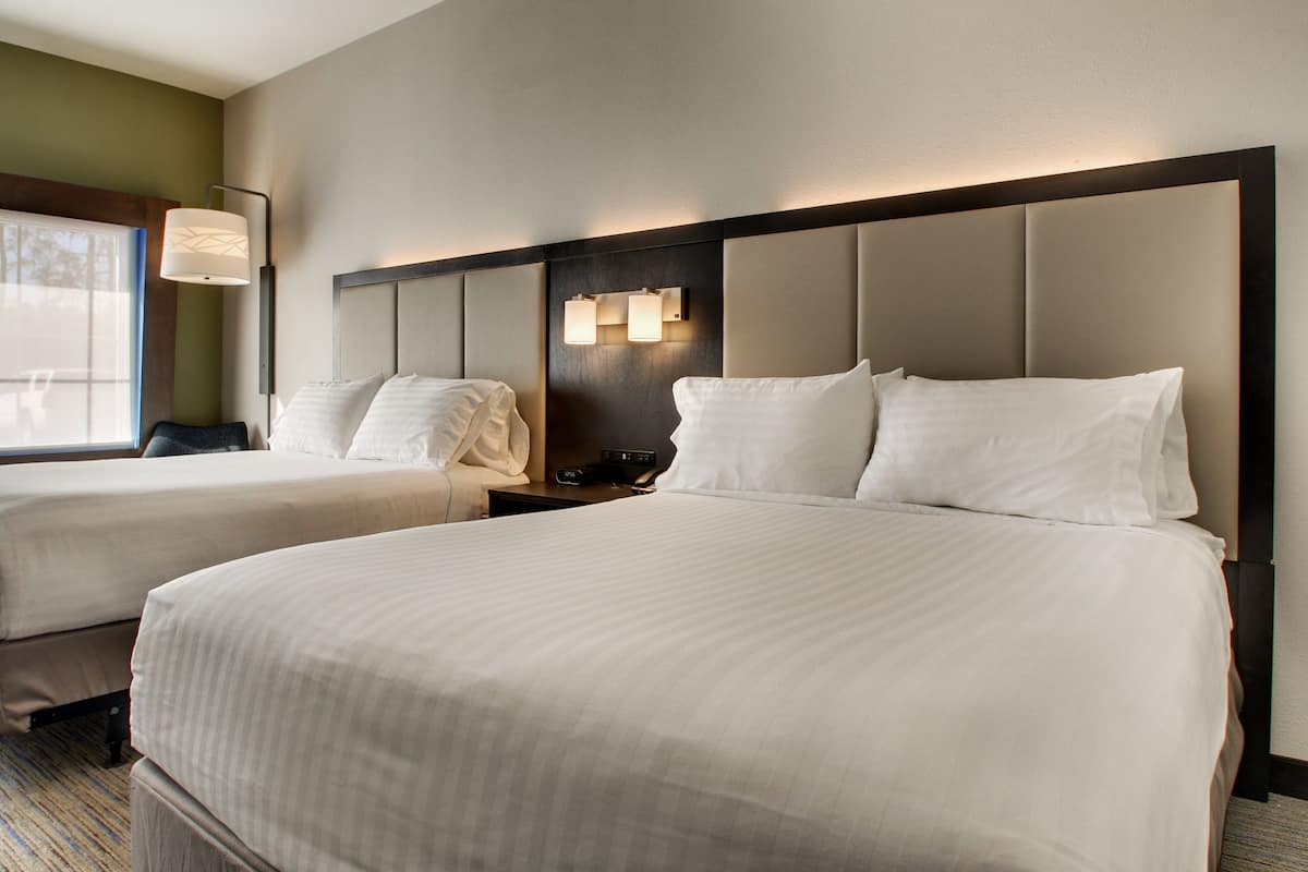 A hotel room with two beds, a nightstand, a lamp, and a window with a view.