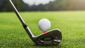 Une balle de golf posée sur un support, avec un club de golf à proximité.