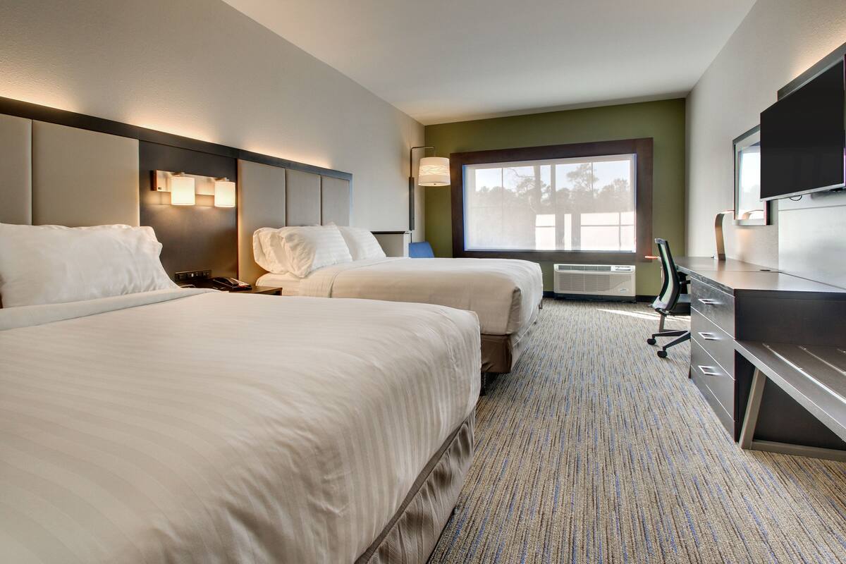 A hotel room with two beds, a desk, a chair, a TV, and a window with a view.