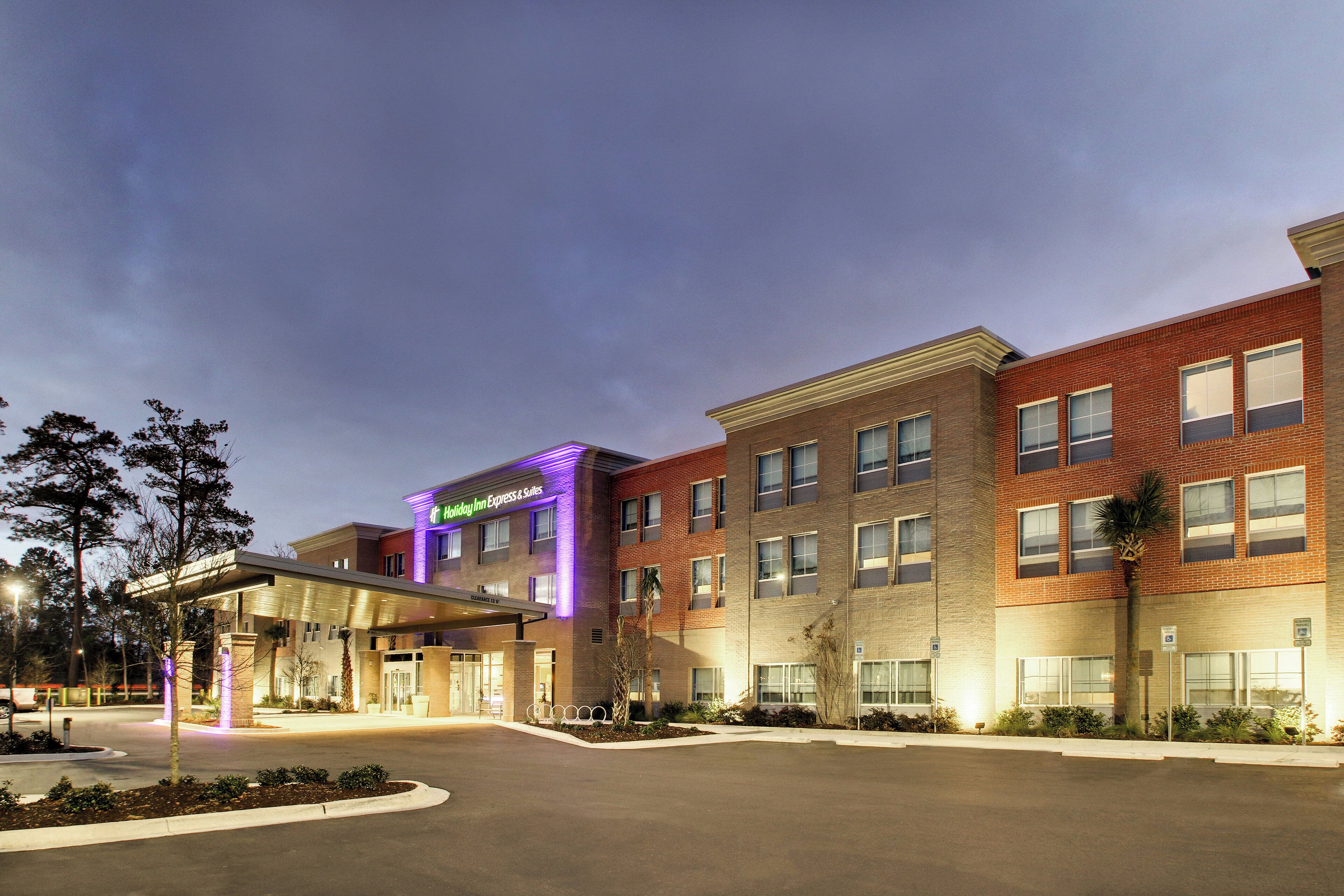 Edificio de Holiday Inn Express & Suites con entrada despejada, zona de estacionamiento y fachada bien iluminada.