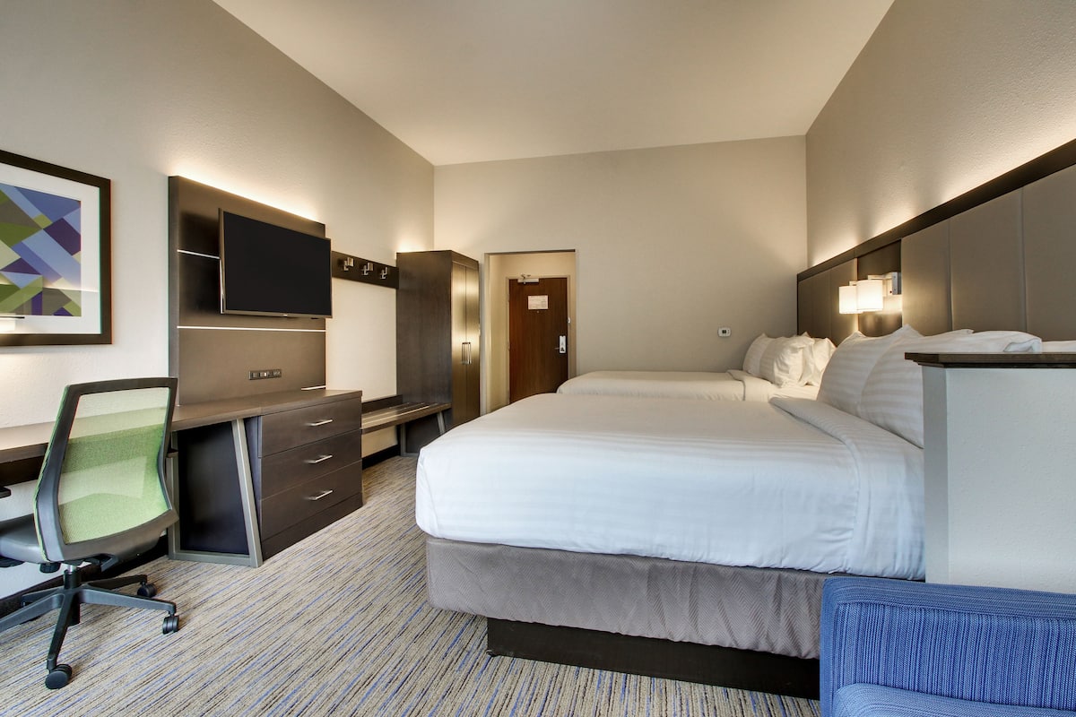 A hotel room with a bed, a desk, a chair, a television, and a door.