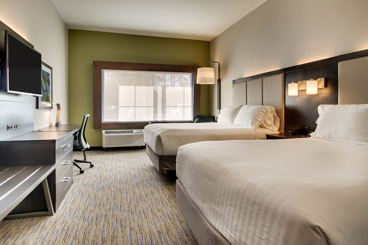 A hotel room with two beds, a desk, a TV, and a window with blinds.