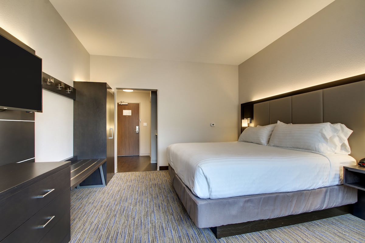 A modern hotel room with a large bed, a flat-screen TV, a desk, and a walk-in closet.