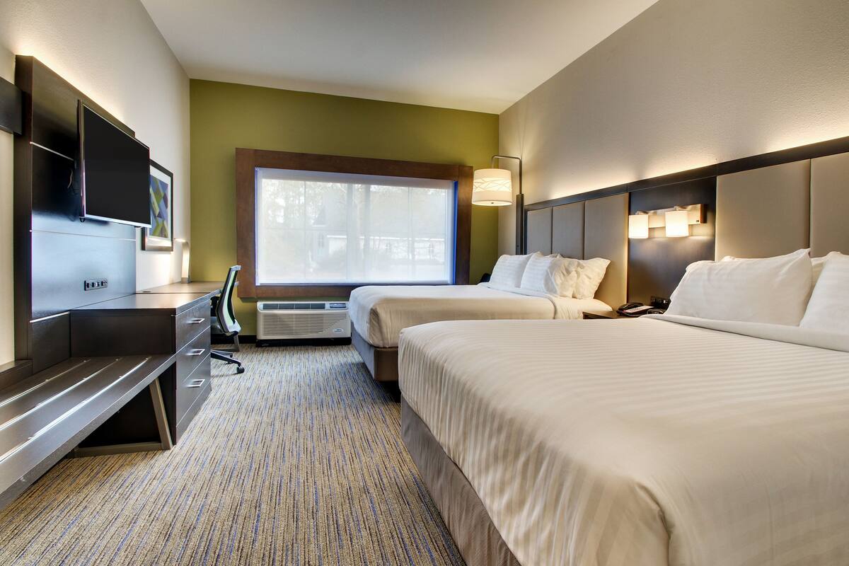 A hotel room with two beds, a desk, a TV, and a window with a view of trees.