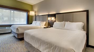 A hotel room with two beds, a large window, and a wall-mounted lamp.