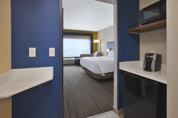A hotel room with a bed, a microwave, a coffee maker, and a view of the city through the window. - Holiday Inn Express Auburn Hills South by IHG (Auburn Hills)