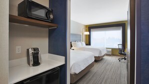 Une chambre d’hôtel équipée d’un four à micro-ondes posé sur une étagère, d’une machine à café, de deux lits, d’un bureau et d’une chaise.