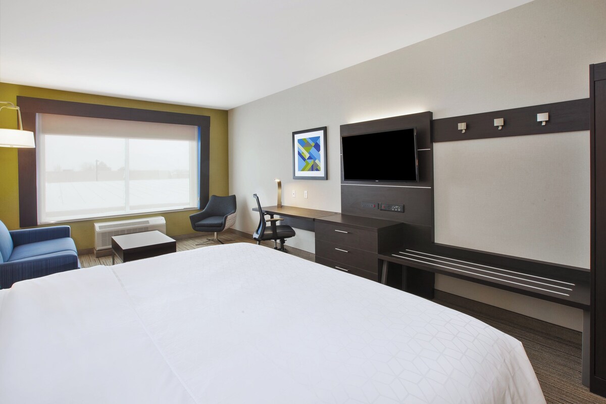 A hotel room with a large bed, a desk, a chair, a flat-screen TV, and a window with blinds.
