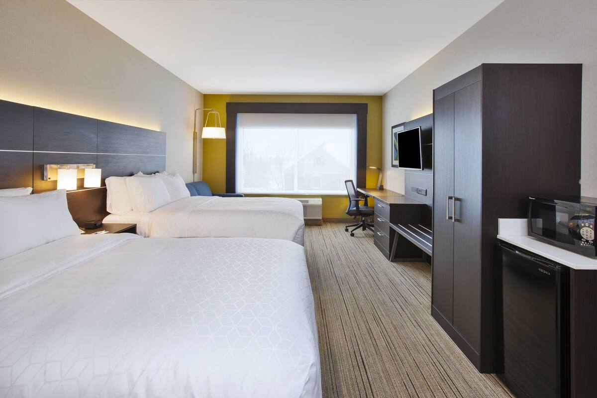 A hotel room with two beds, a desk, a television, and a minibar.
