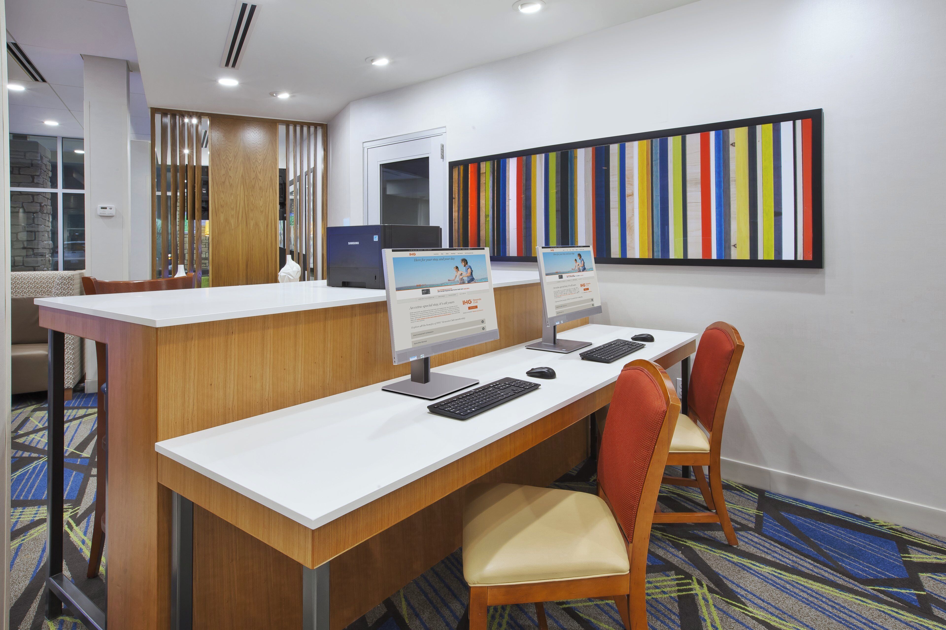Un comptoir d’accueil d’hôtel équipé d’ordinateurs, agrémenté d’une grande œuvre d’art colorée et doté d’un sol recouvert de moquette.