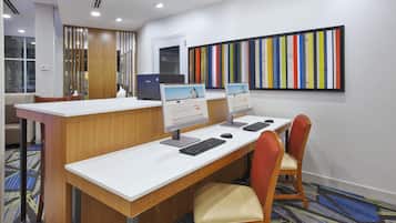 A hotel reception desk with computers, a large colorful artwork, and a carpeted floor.