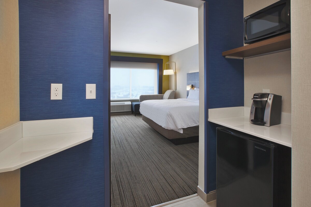 A hotel room with a bed, a microwave, a coffee maker, and a view of the city.