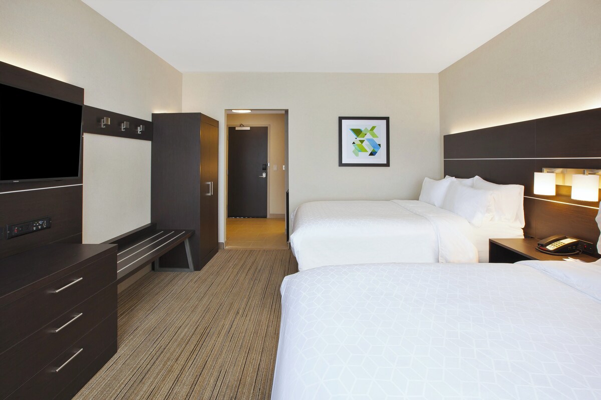 A hotel room with a flat-screen TV, a desk with a phone, two beds, a dresser, and a framed picture on the wall.