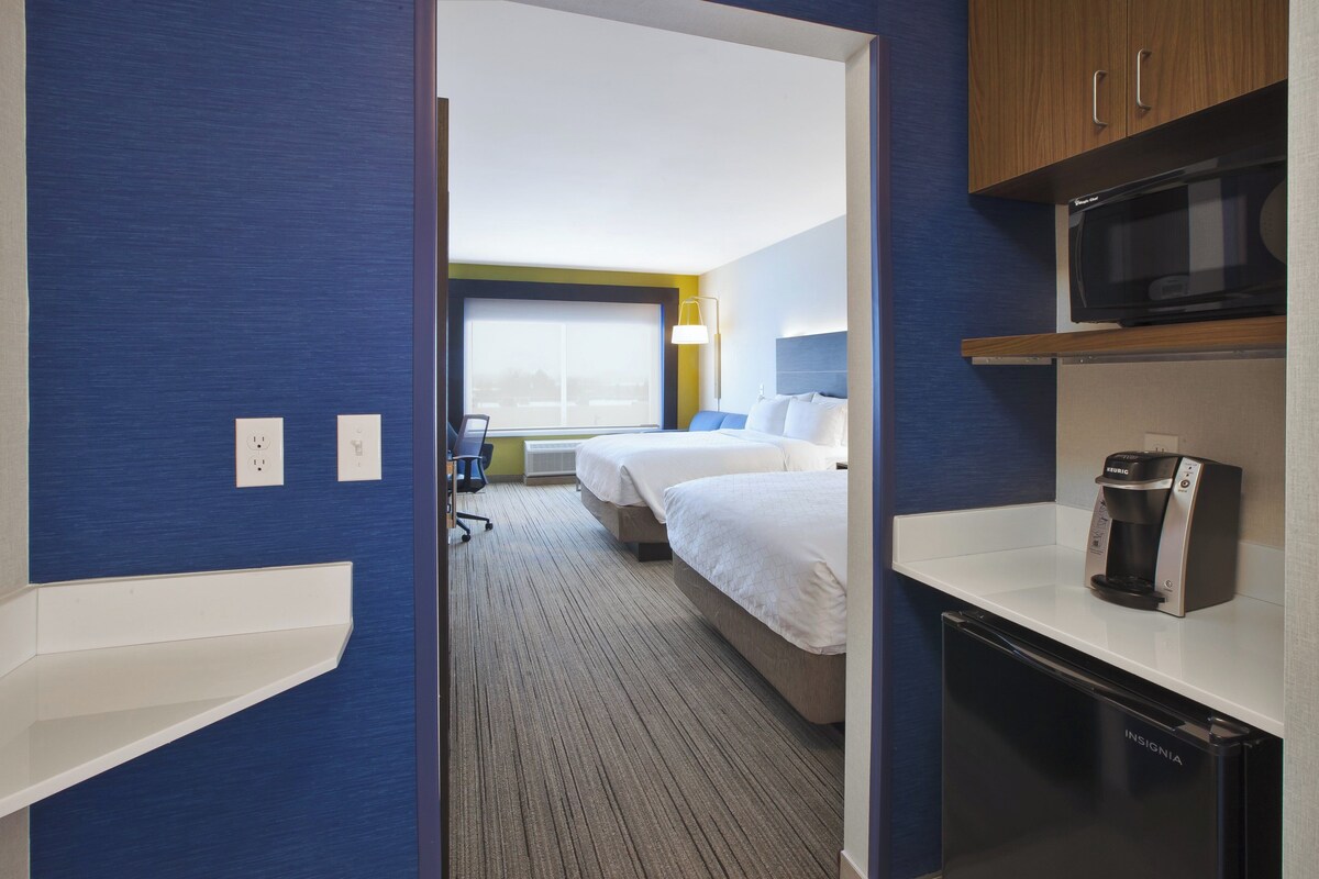 A hotel room with a kitchenette, a bed, a desk, and a window.