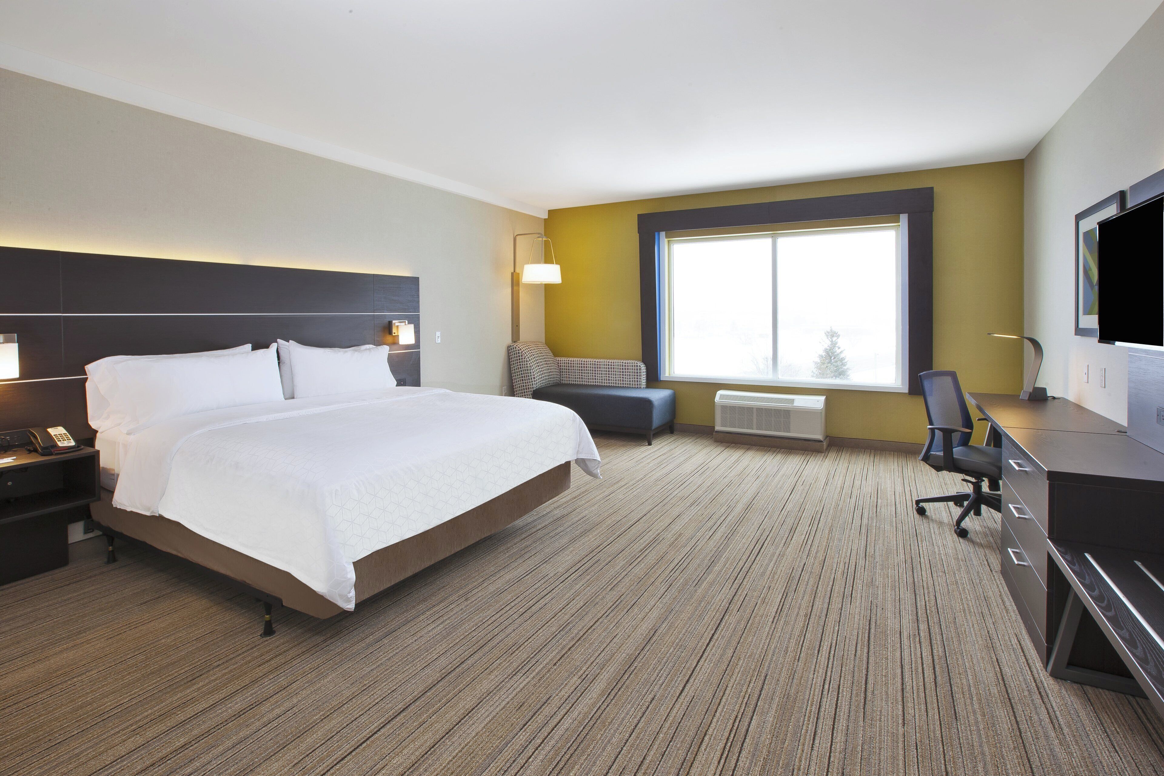 A hotel room with a bed, bedside tables, a desk with a chair, a television, and a large window.