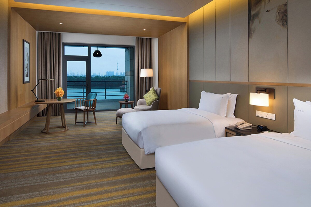 A hotel room with two beds, a desk, a chair, and a view of a body of water.