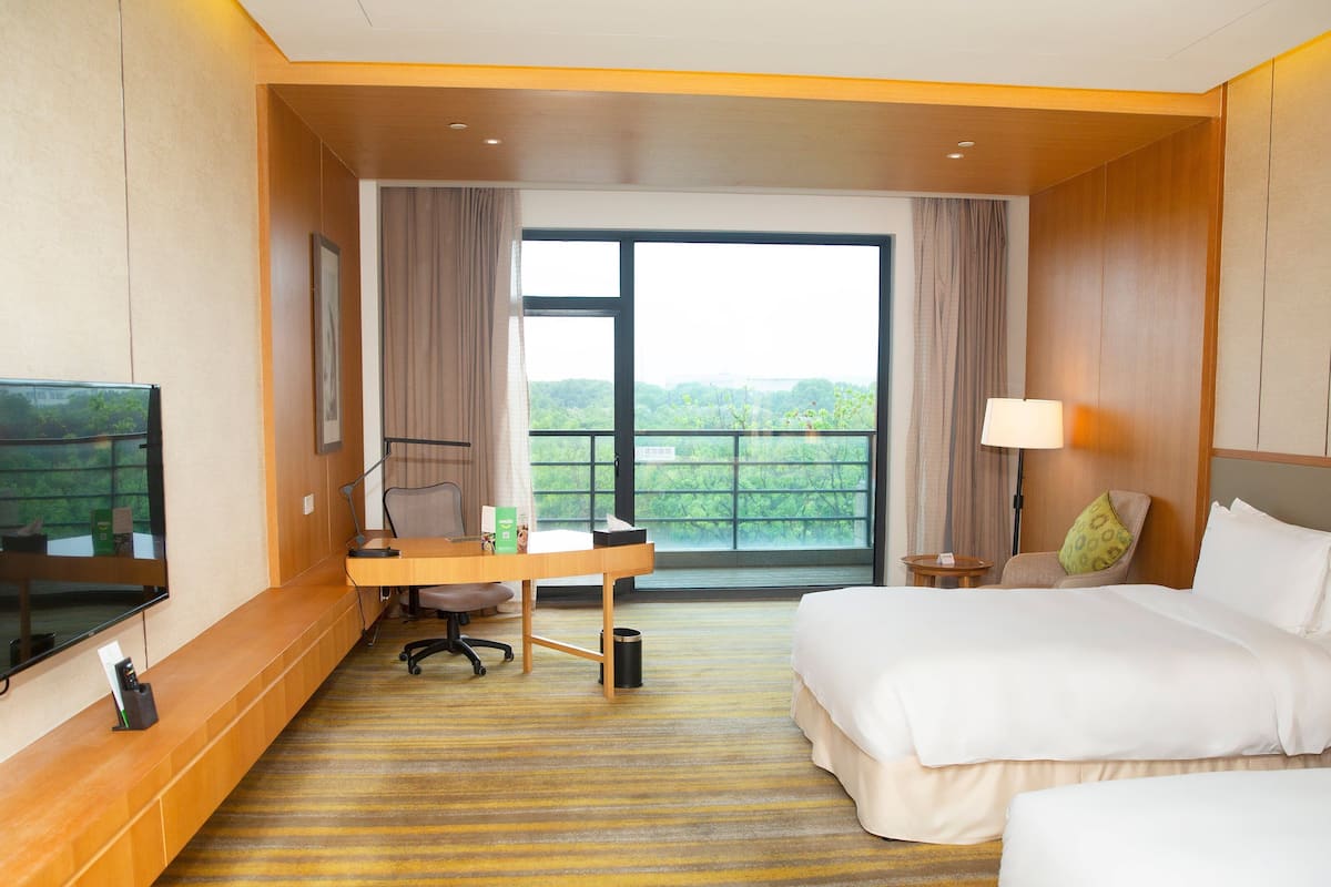 Habitación de hotel con una cama, un escritorio con silla, un televisor montado en la pared y una ventana con cortinas.