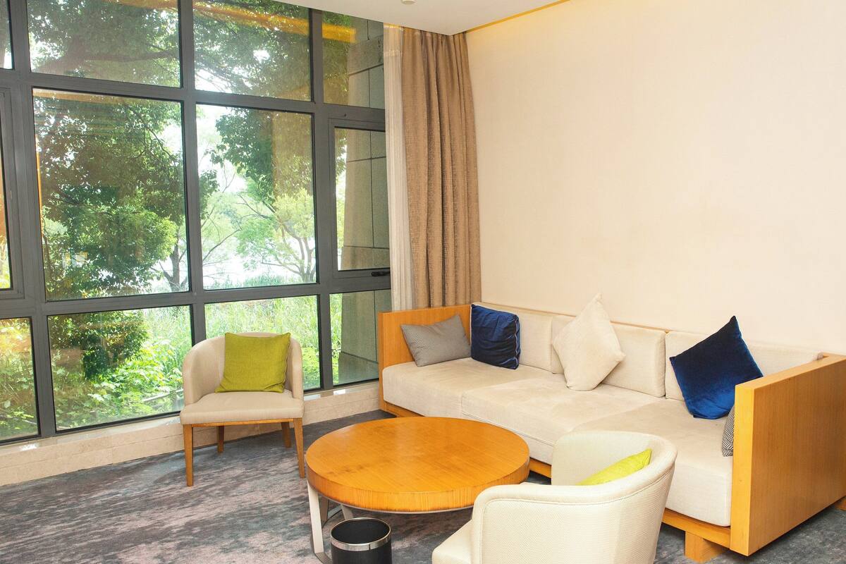Una habitación de hotel moderna con un ventanal grande, un conjunto de sofá, una mesa de centro redonda y una silla.