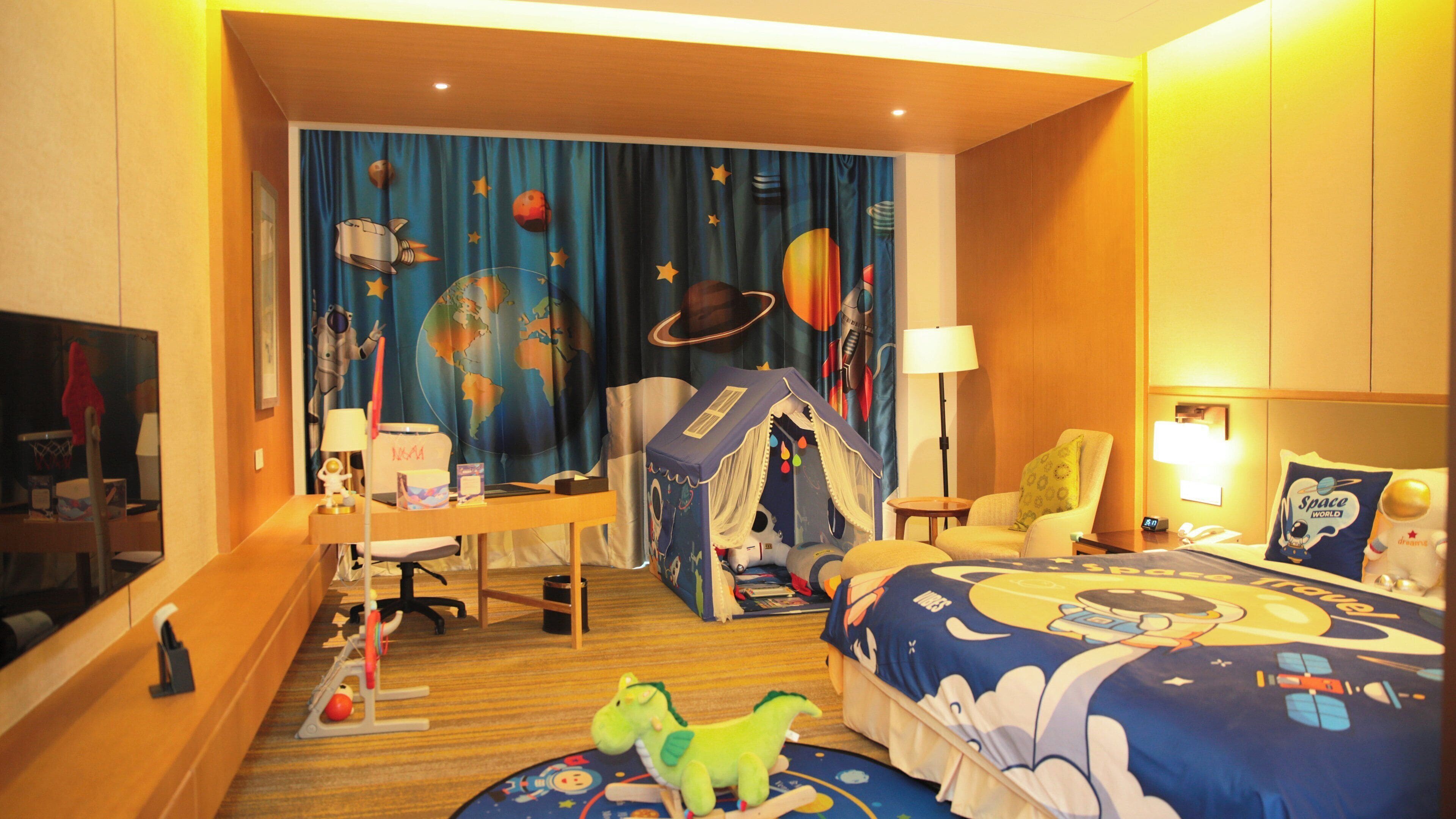 A hotel room with a bed, desk, chair, and a play tent.