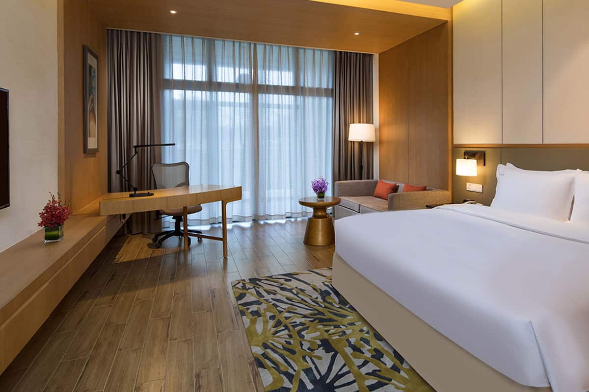 A hotel room with a large bed, a desk, a chair, a sofa, and a small table with a lamp.