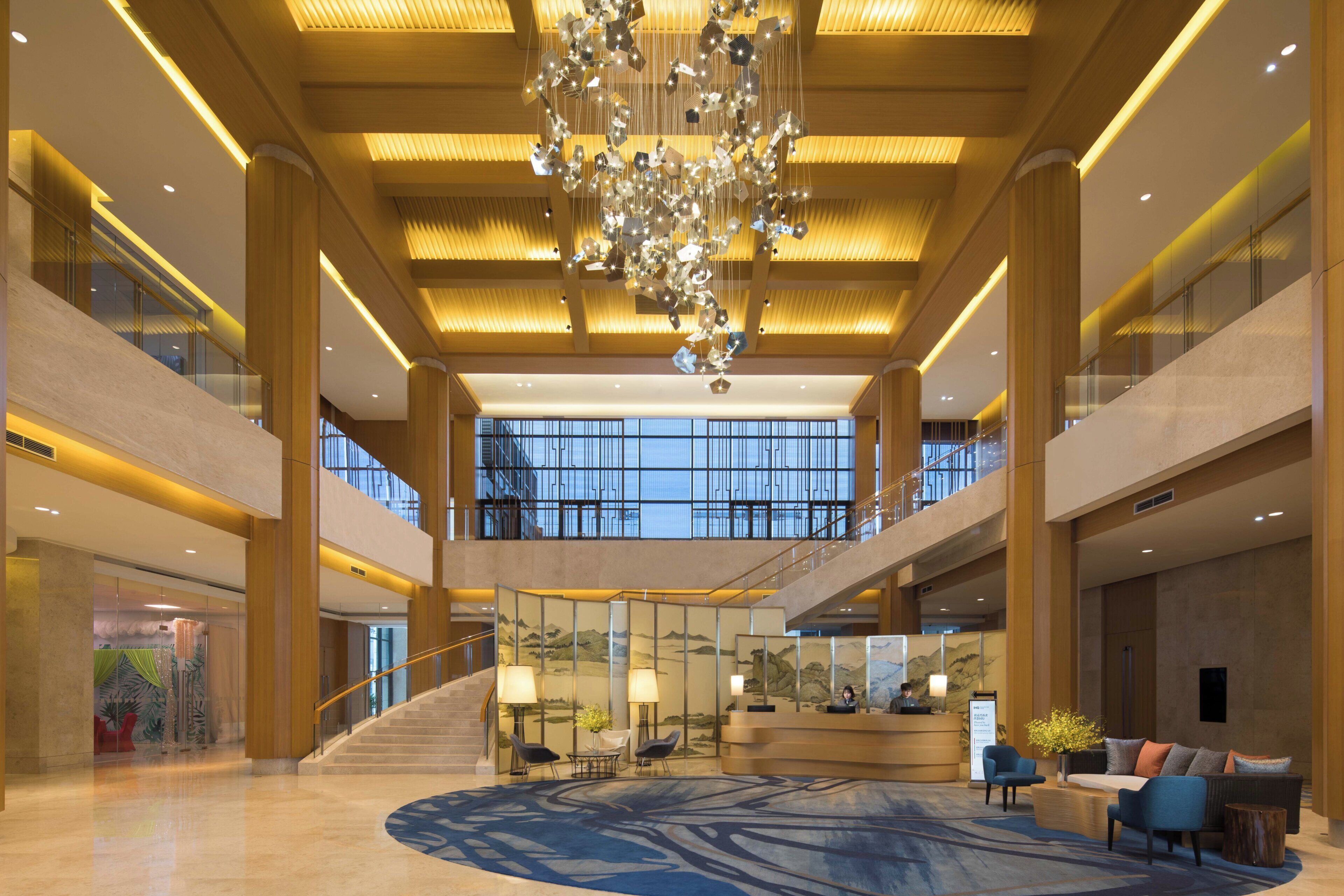 A spacious lobby with a grand chandelier, a reception desk, and a staircase leading to upper floors.