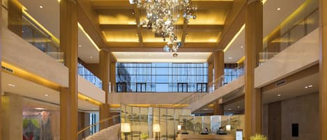 A spacious lobby with a grand chandelier, a reception desk, and a staircase leading to upper floors.