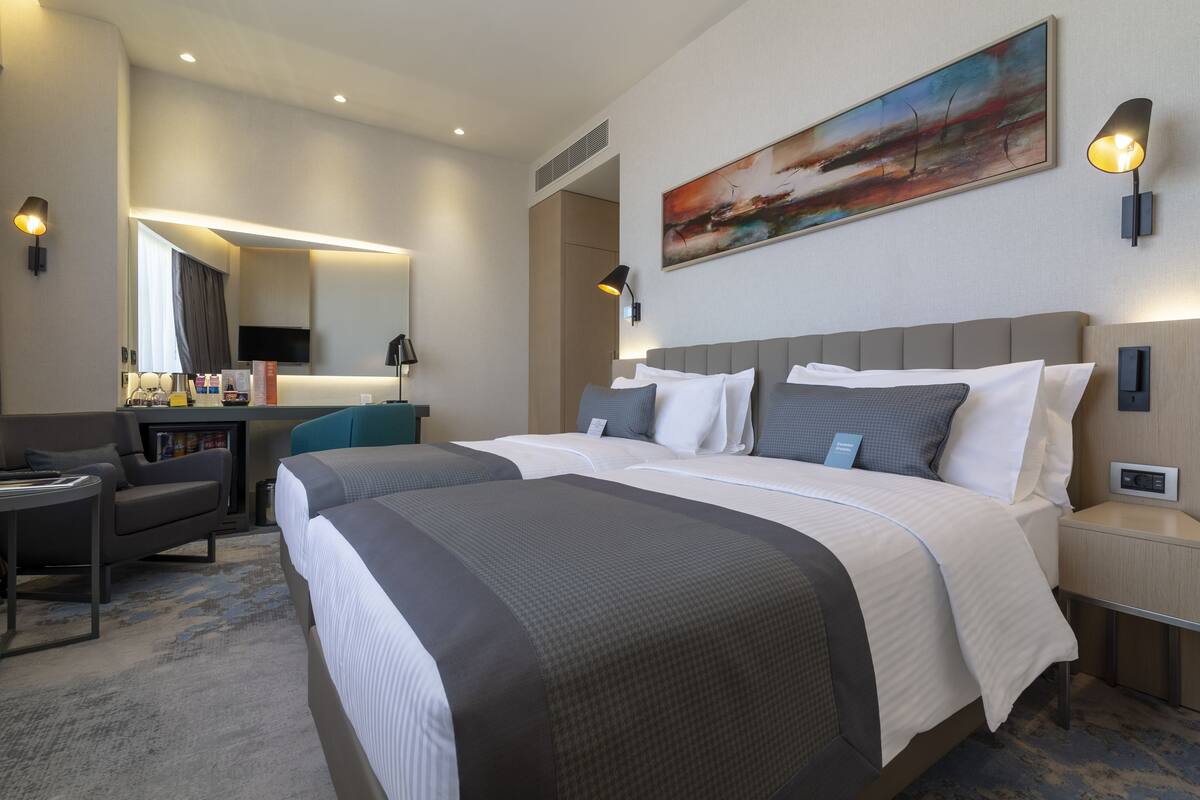 Une chambre d’hôtel avec deux lits, un bureau, une chaise, une télévision et des œuvres d’art accrochées au mur.