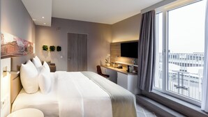 Habitació d'hotel moderna amb un llit gran, escriptori, cadira, televisió i finestra amb vista a la ciutat.