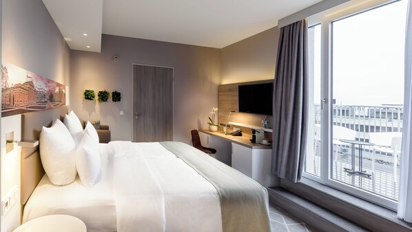 A modern hotel room with a large bed, a desk, a chair, a TV, and a window with a city view. - Holiday Inn Express Munich - City East by IHG (Munich)