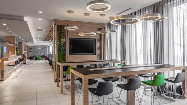 Un interior modern amb una taula de dinar llarga, molta cadira, zona de bar i un televisor pla gran.