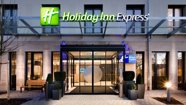 Exterior d'un hotel Holiday Inn Express de disseny modern, amb una entrada destacada amb portes de vidre i un senyal digital que mostra el nom de l'hotel.