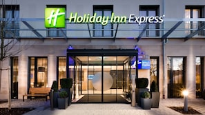 The exterior of a Holiday Inn Express hotel with a modern design, featuring a prominent entrance with glass doors and a digital sign displaying the hotel name. - Holiday Inn Express Munich - City East by IHG (Munich)