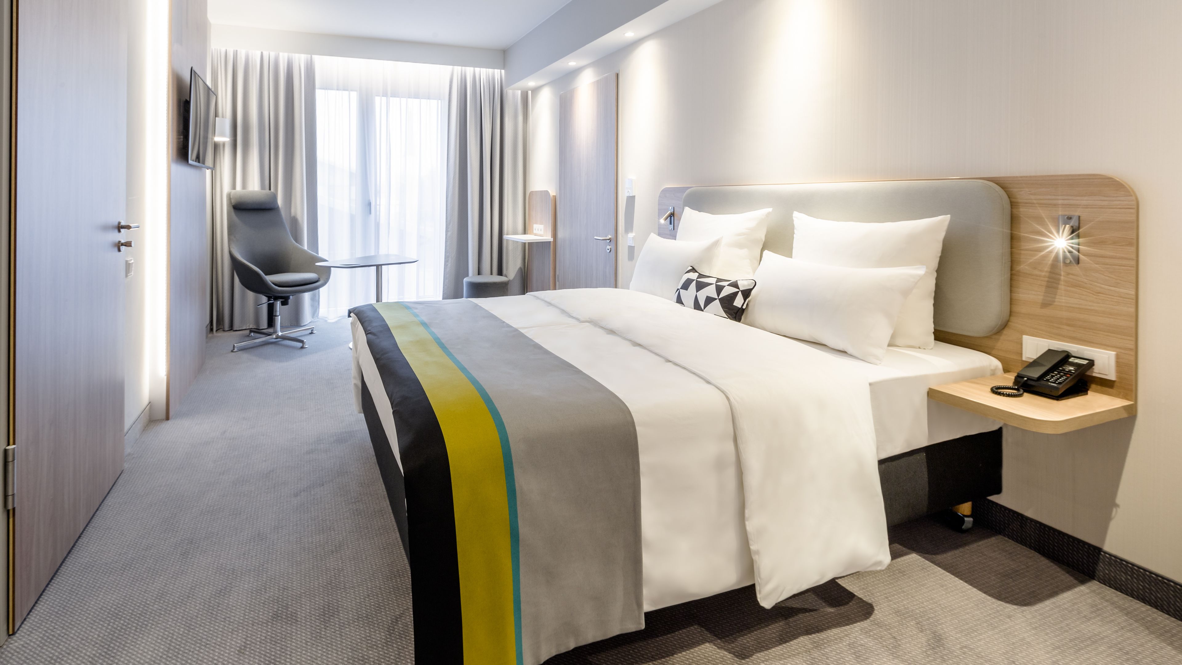 Een hotelkamer met een bed, nachtkastje, stoel en een bureau met telefoon.