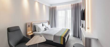 Una habitación de hotel moderna con cama, escritorio, silla, televisión y ventana con cortinas.