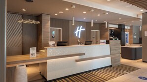 Una zona d'entrada d'hotel moderna amb un taulell de recepció de fusta, un senyal de neó i un pantalla digital.