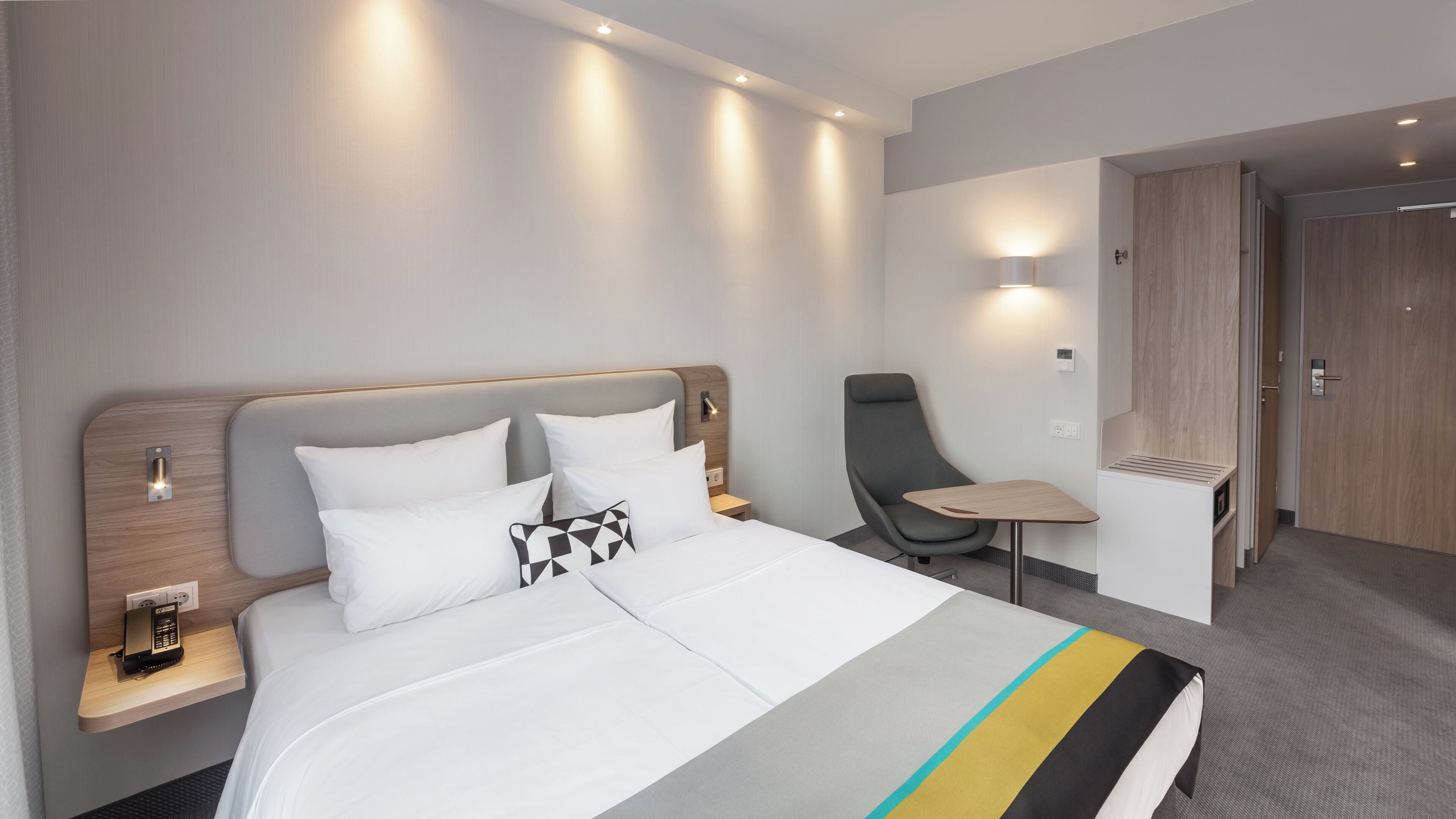 Una habitación de hotel con cama, mesita de noche, silla y un pequeño escritorio.