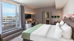 A hotel room with a bed, a desk, a TV, a bathroom, and a balcony with a view of the city. - Holiday Inn Express Munich - City East by IHG (Munich)