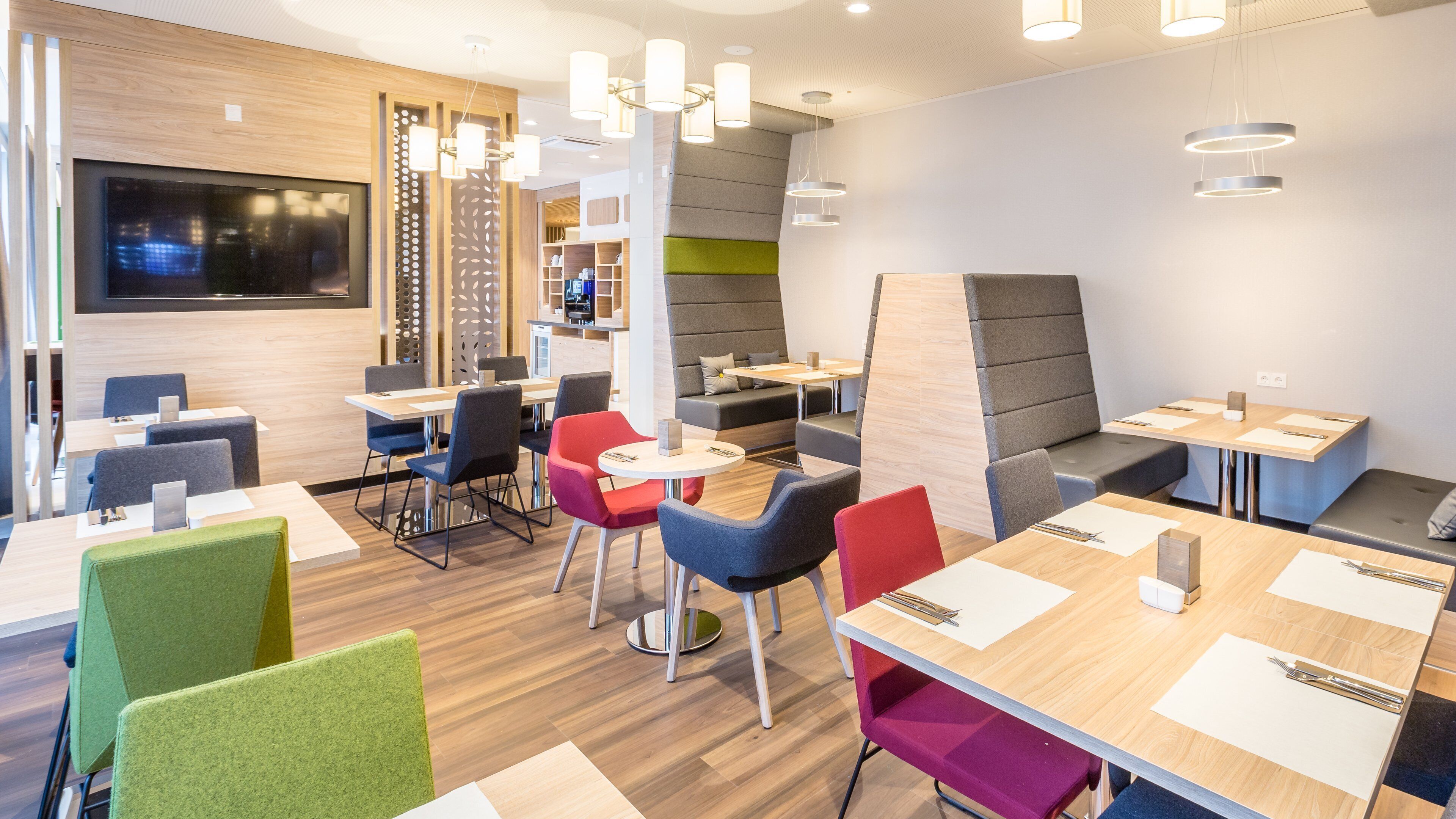 Ein modernes Restaurant mit Holzböden, mehreren Sitzbereichen wie Sitzecken und Tischen, sowie zeitgemäßen Beleuchtungselementen.