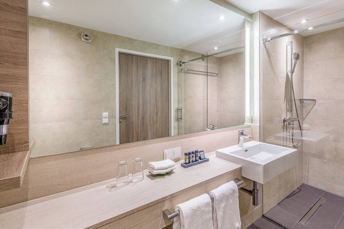Une salle de bain moderne avec un grand miroir, deux lavabos, une douche et une machine à café.