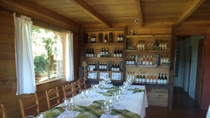 Una larga mesa de comedor dispuesta con copas de vino y menús, rodeada de sillas de madera, con botellas de vino en estanterías al fondo.