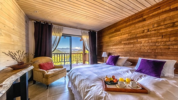 Un dormitorio con una cama grande, una pared de madera, vistas a las montañas y una bandeja de desayuno sobre la cama.