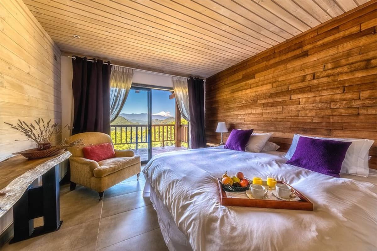 Une chambre avec un grand lit, un mur en bois, une vue sur les montagnes et un plateau de petit-déjeuner posé sur le lit.