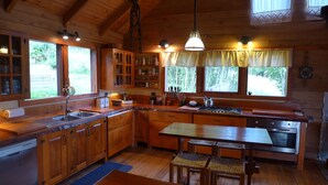 Cocina de cabaña de madera con una mesa, sillas, un lavabo, armarios y una estufa.
